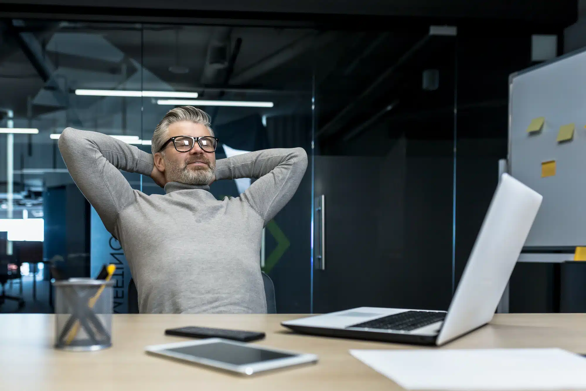 Senior gray haired man resting in office on chair with hands behind head, businessman boss working