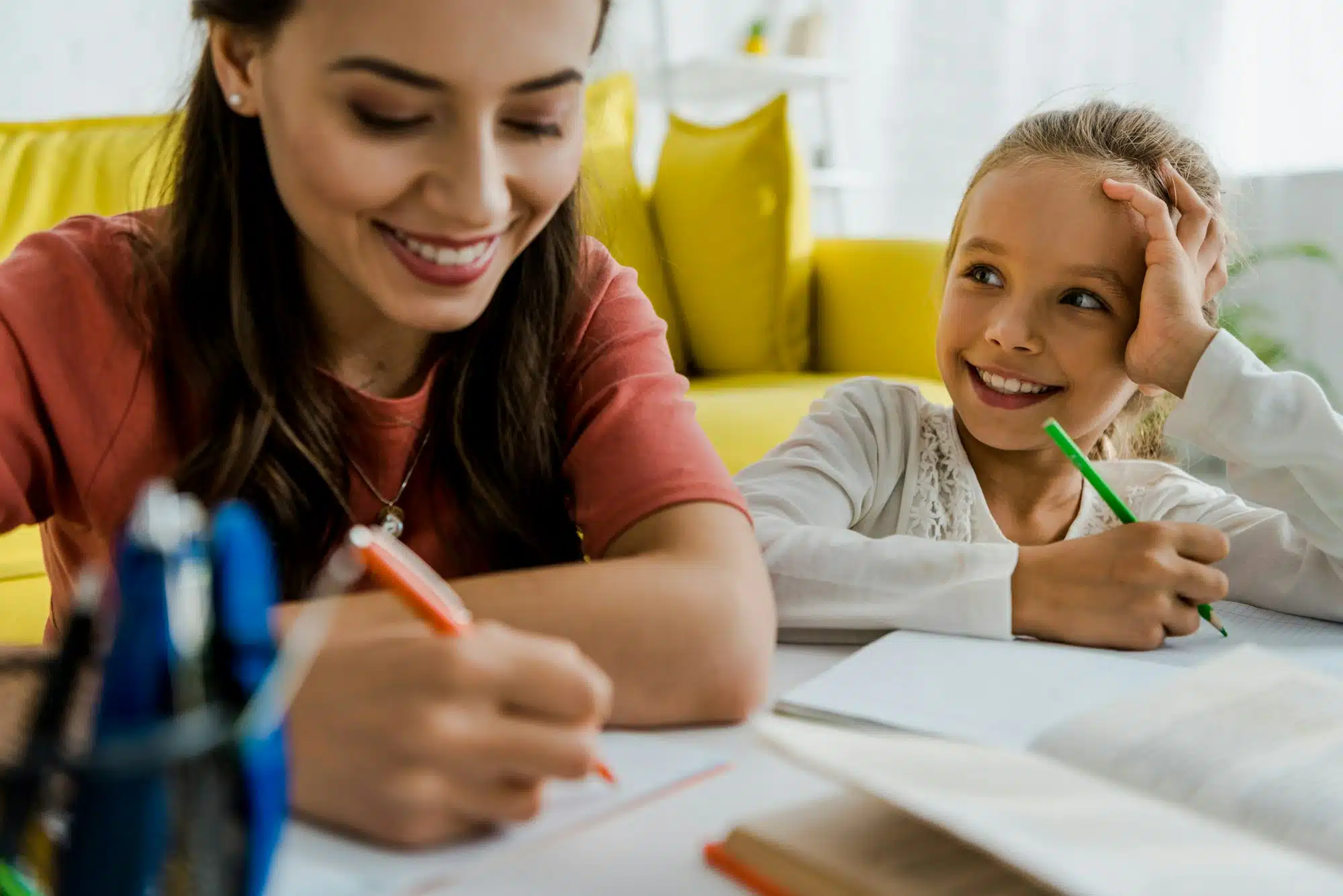 selective focus of happy kid looking at cheerful babysitter holding pen in living room