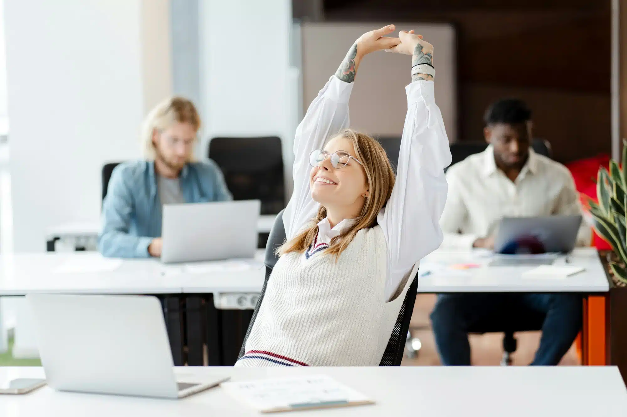 Happy businesswoman stretching at workplace with laptop on desk