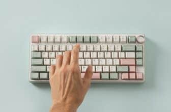 Female hand typing on keyboard on blue background. View from above. Flat lay.