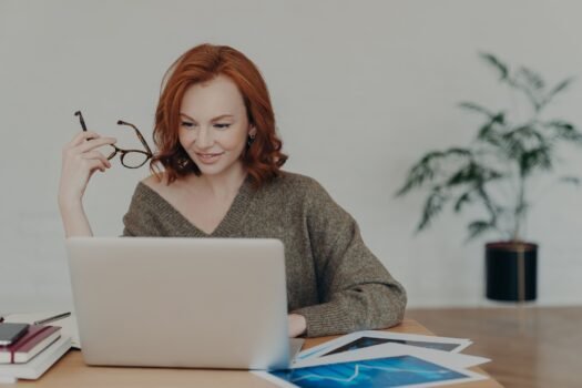 Busy redhead adult woman does freelance work on laptop computer, focused in monitor