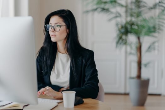 Elegant brunette businesswoman poses at cowroking space, concentrated at monitor of computer