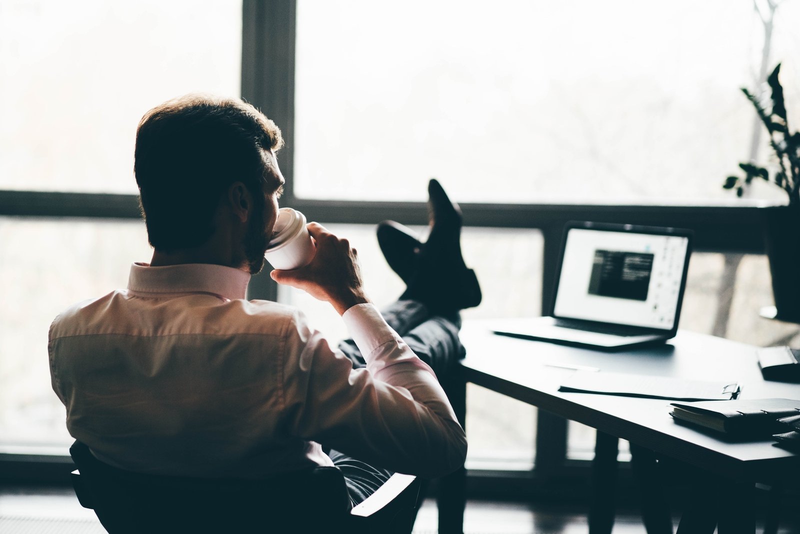 Businessman drinking coffee in the break. Silhouette man sitting with feet on table and resting.